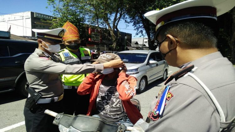 Petugas Satlantas Polresta Padang memakaikan masker kepada pengendara yang tak menggunakan masker saat melintas di depan Kantor Laka Lantas. (IST)