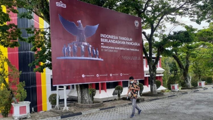 Seorang pria berjalan di depan Baliho peringatan Hari Kesaktian Pancasila yang dipasang di Plaza Kantor Pusat PT Semen Padang, Jumat (1/10/2021). Manajemen PT Semen Padang mengajak seluruh karyawan Semen Padang Group untuk mengibarkan bendera setengah tiang pada tanggal 30 September dan bendera satu tiang pada 1 Oktober 2021.