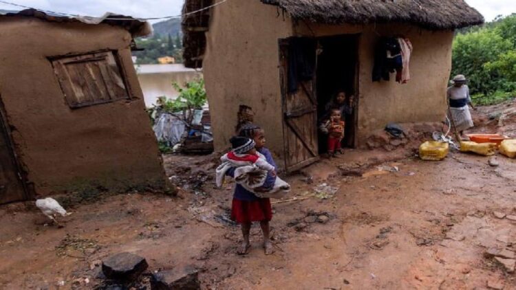 Seorang bocah menggendong bayi di luar rumah yang rusak di daerah banjir, saat Topan Batsirai menyapu daratan, di Fianarantsoa, Madagaskar, 6 Februari 2022. (REUTERS/Alkis Konstantinidis)