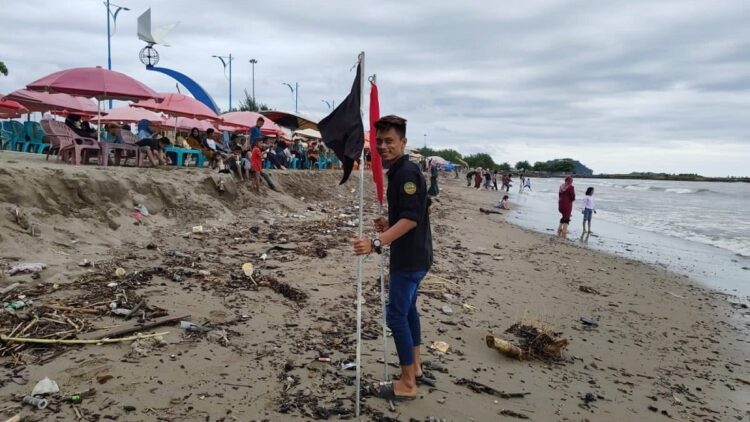 Antisipasi Keselamatan Pengunjung, Dispar Pasang Bendera Peringatan di Pantai Padang 1 Seorang petugas memasang bendera peringatan di sepanjang Pantai Padang. (Istimewa)
