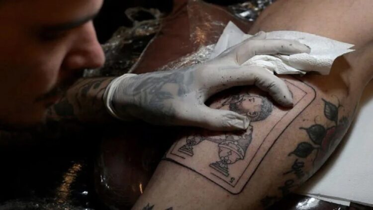 Sukses jadi Juara Piala Dunia, Fan Argentina Antre bikin Tato Messi 1 Seniman tato Tebi Cobra Vucinovich asal Argentina mengerjakan tato bergambar kapten tim nasional Argentina Lionel Messi mencium trofi Piala Dunia FIFA di kaki Ariel Sacchi di Ds Tatto Shop, Buenos Aires, Argentina. (23/12/2022) (AFP/JUAN MABROMATA)