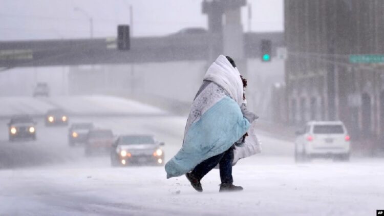 Seseorang yang terbungkus selimut melintasi jalan yang tertutup salju pada Kamis, 22 Desember 2022 di AS. (Foto AP/Jeff Roberson)