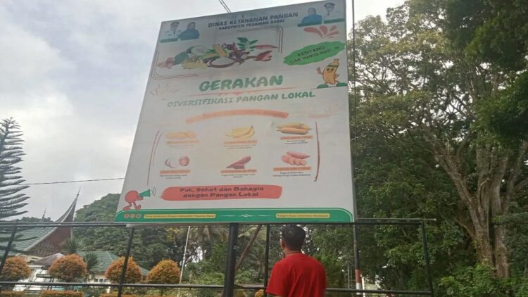 Seorang warga memperhatikan baliho ajakan dari Pemkab Pasaman Barat untuk sosialisasi gerakan diversifikasi pangan lokal di daerah itu, Jumat (6/10/2023). Antara/Altas Maulana.
