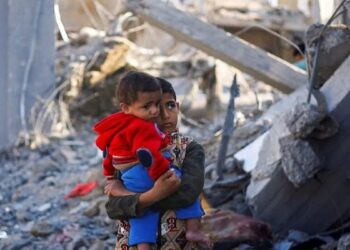 Seorang anak laki-laki Palestina sambil menggendong balita berdiri di lokasi serangan Israel saat konflik yang sedang berlangsung antara Israel dan kelompok perlawanan Palestina Hamas di Rafah, di selatan Jalur Gaza, Senin (4/12/2023). (ANTARA FOTO/REUTERS/Mohammed Salem/Spt.)