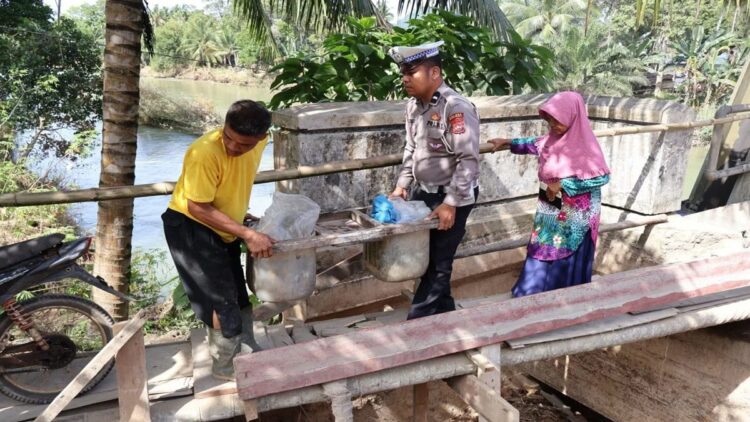 Seorang polisi membantu warga melintasi jembatan darurat di Kabupaten Pesisir Selatan yang terdampak banjir dan tanah longsor. (ANTARA/Muhammad Zulfikar).